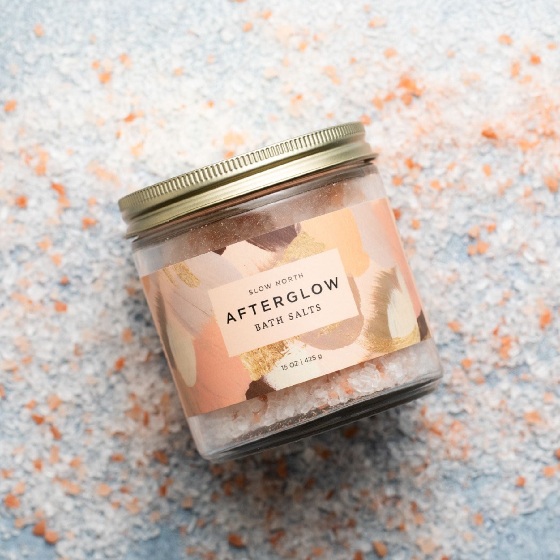 Jar of 'Afterglow' bath salts on a textured surface with small orange and white specks.