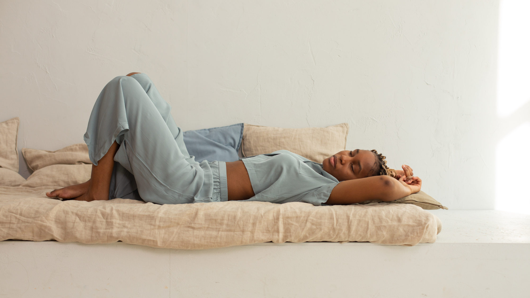 woman lays on a mattress daybed with arms folded overhead