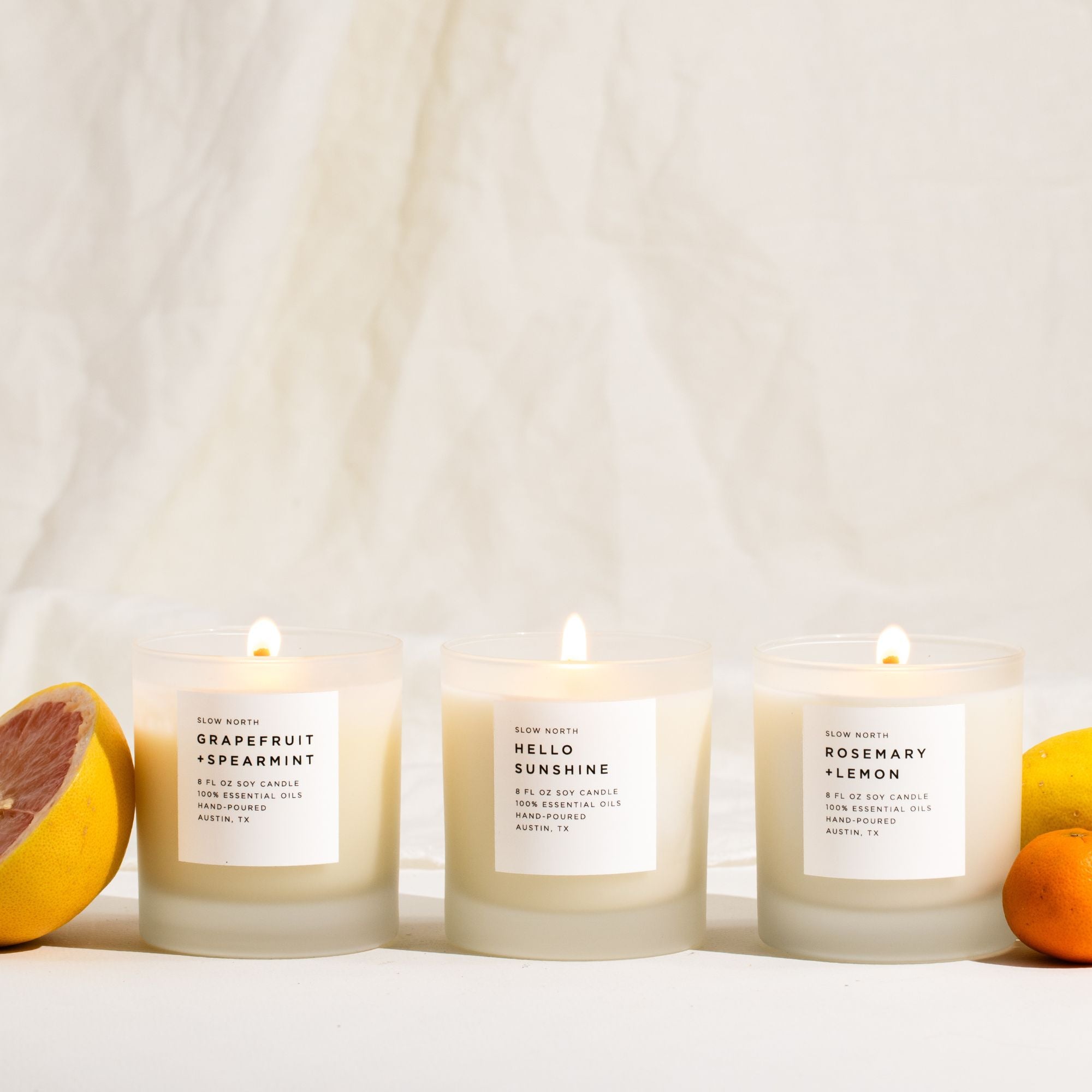 Three lit candles with labels on a white background, surrounded by fruits.