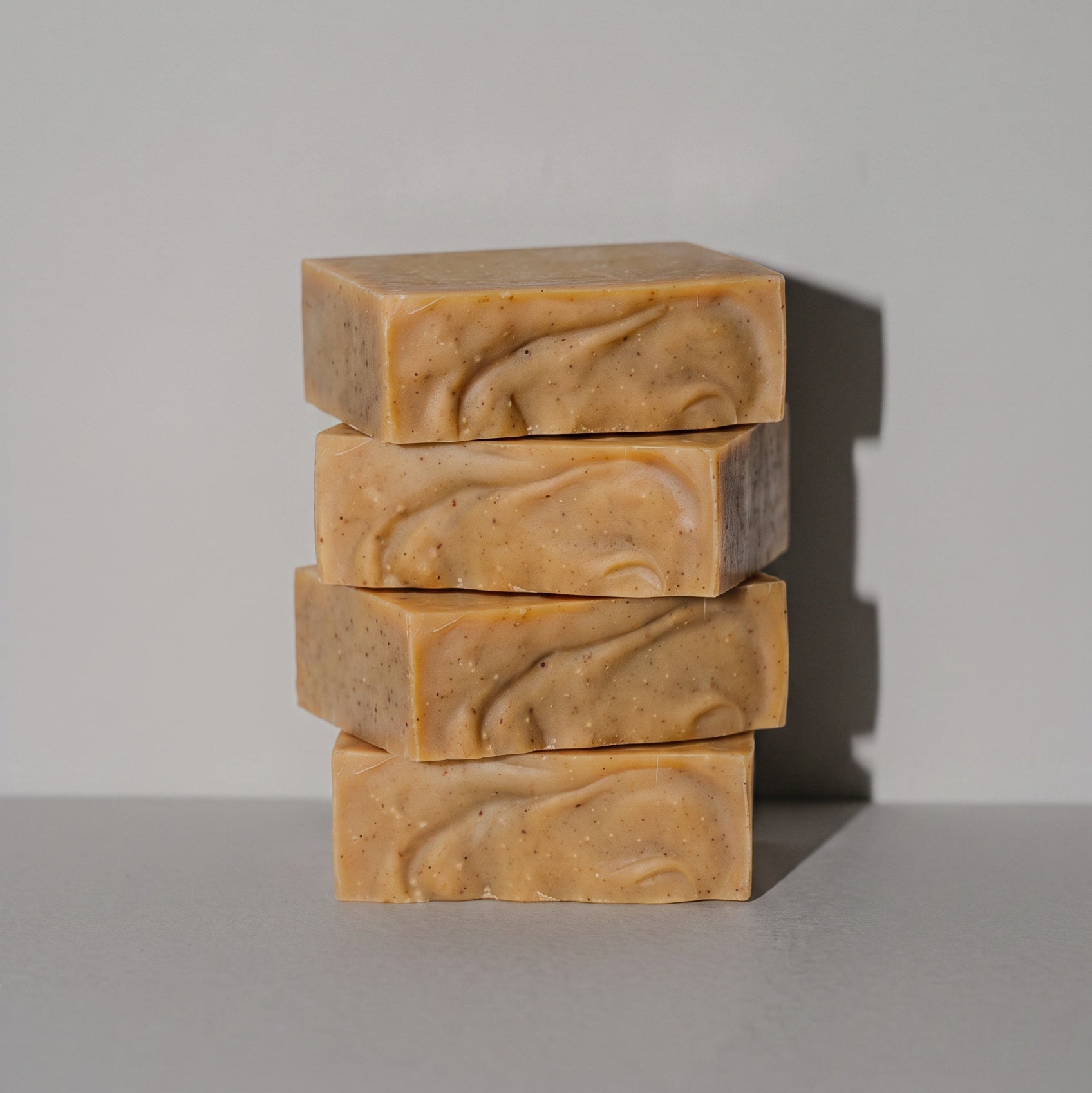 Four stacked rectangular bars of handmade soap in a warm tan and light brown marbled pattern, set against a plain light gray background.