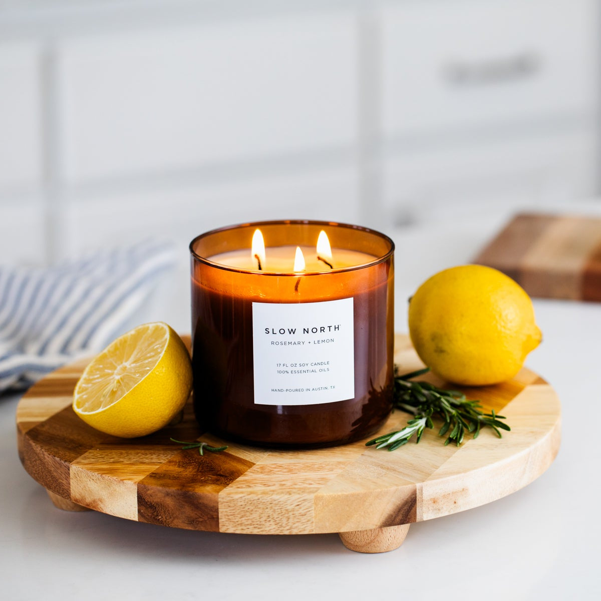 Lit candle on a wooden tray with lemons on a kitchen counter